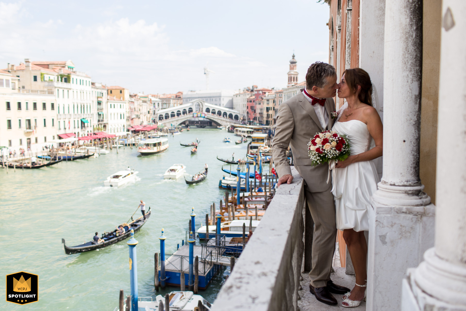Newlyweds Share Balcony Kiss Overlooking Grand Canal at Palazzo Cavalli in Venice A romantic wedding photo captured at Palazzo Cavalli in Venice, featuring a newly married couple sharing a kiss on a balcony overlooking the Grand Canal with gondolas passing by.