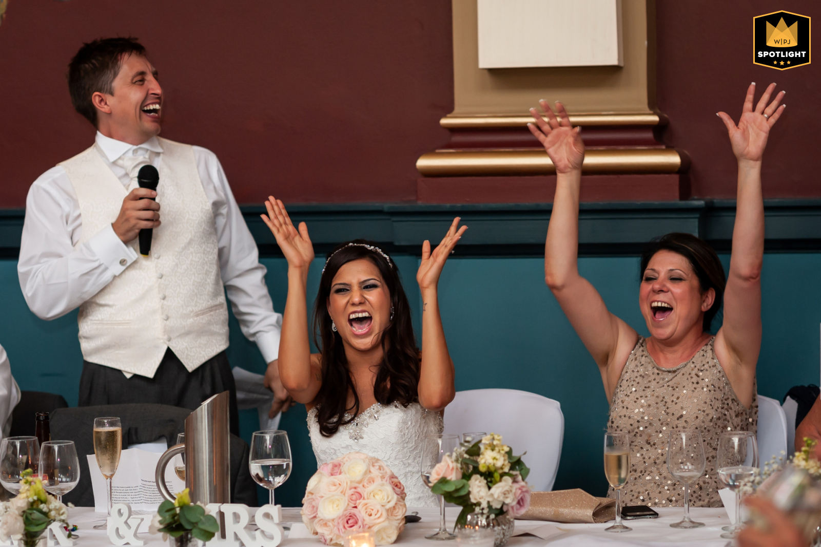 At De Vere Beaumont Estate in Windsor, the bride and her mother enthusiastically cheer during the groom's speech, highlighting the joyous atmosphere of the wedding celebration.