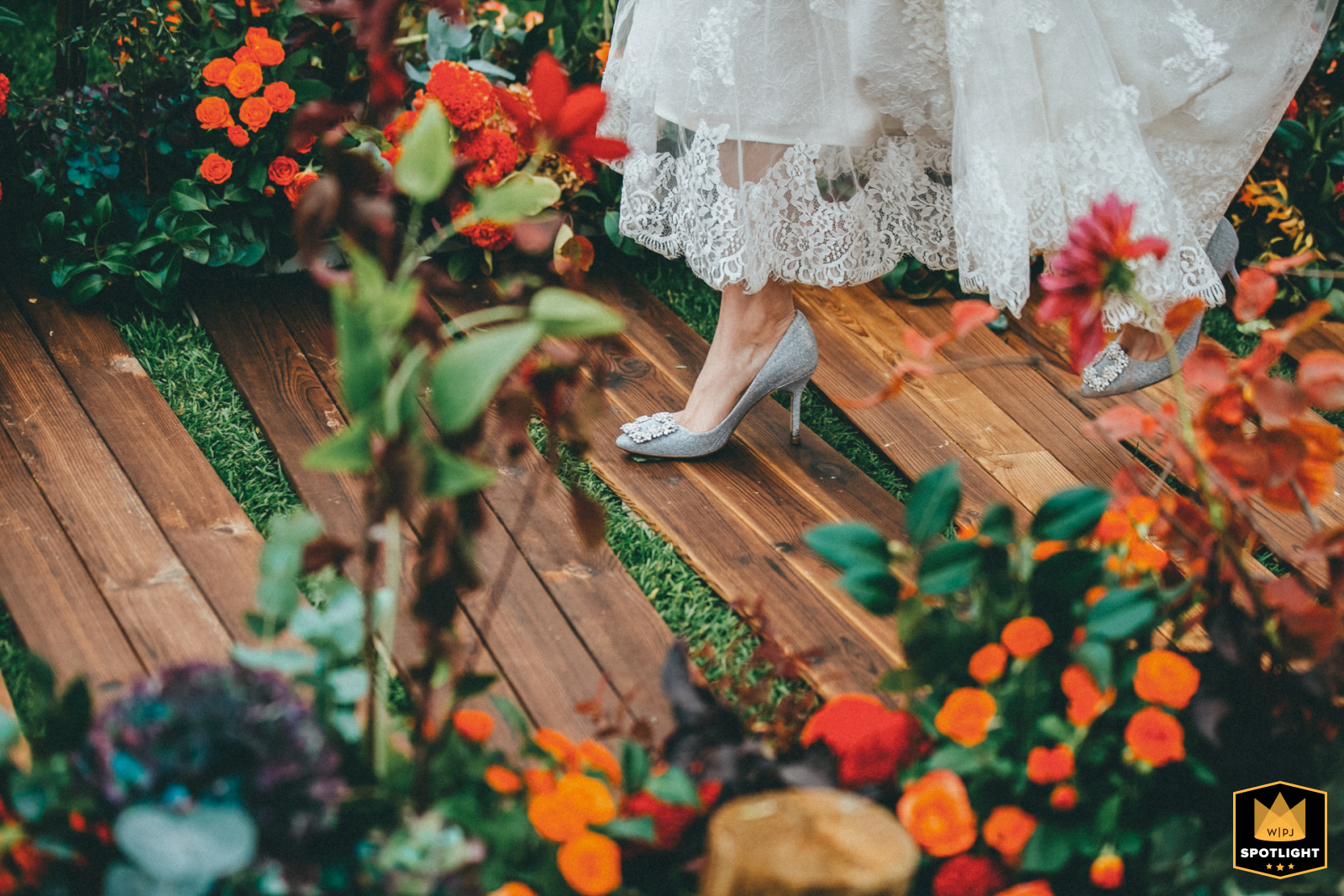 This WPJA Spotlight award-winning image features a stunning detail shot of a bride's foot wearing a delicate shoe as she gracefully walks on wooden planks on the grass at Beijing Hongxi Golf, with a charming border of flowers adorning the edges.