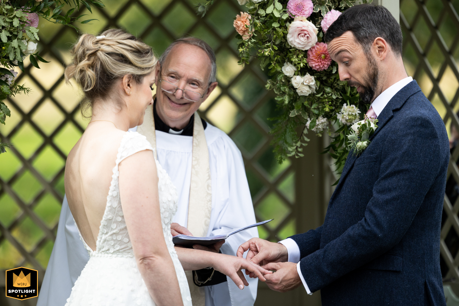 At Longstowe Hall in Cambridge. A playful moment as the groom struggles to slip the ring onto the bride's finger during the outdoor vows.