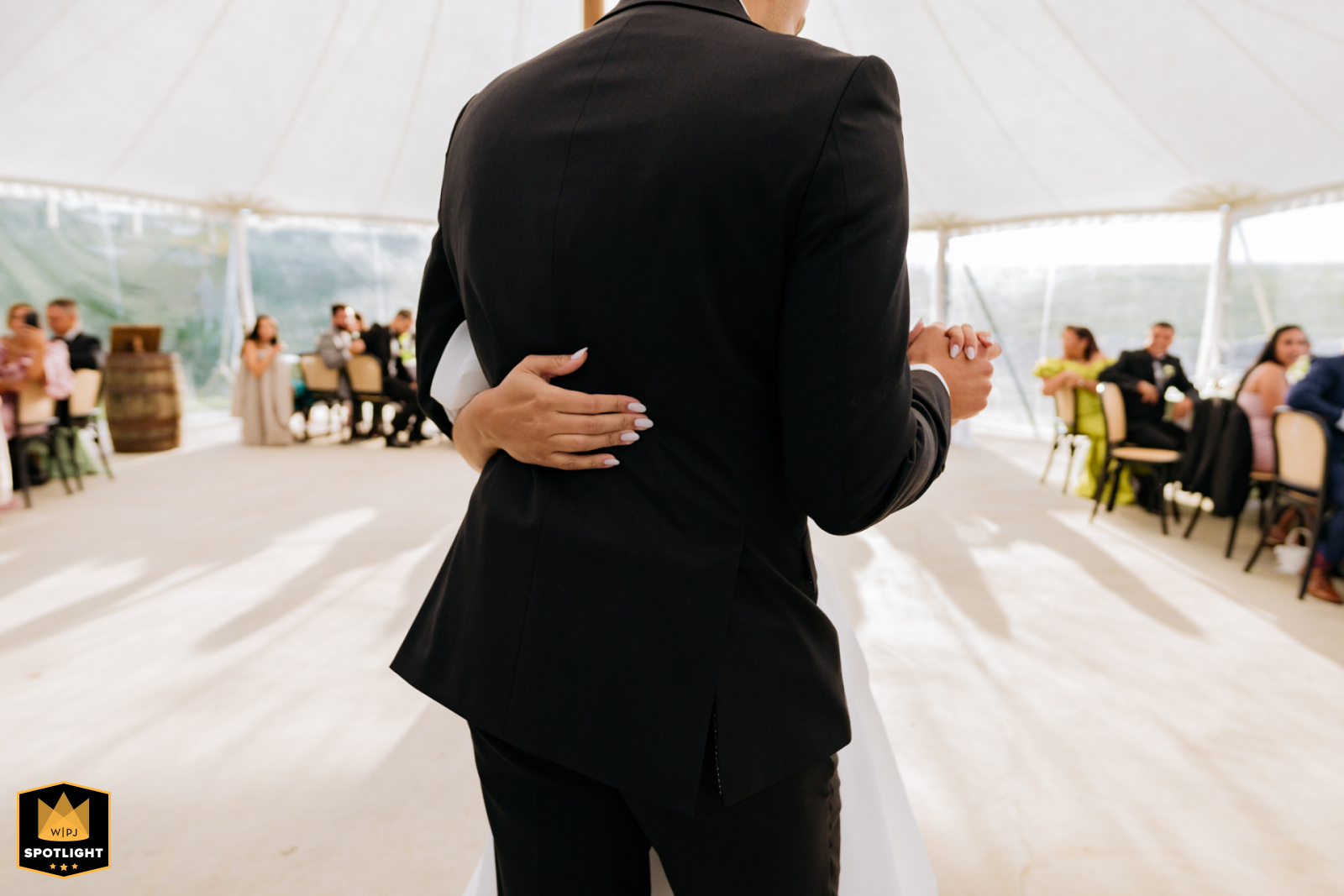 In Toronto, a detailed shot beautifully captures the bride's hands gently resting on the back of the groom's jacket as they dance. The scene, set against a soft white background, highlights the intimacy and connection between them.