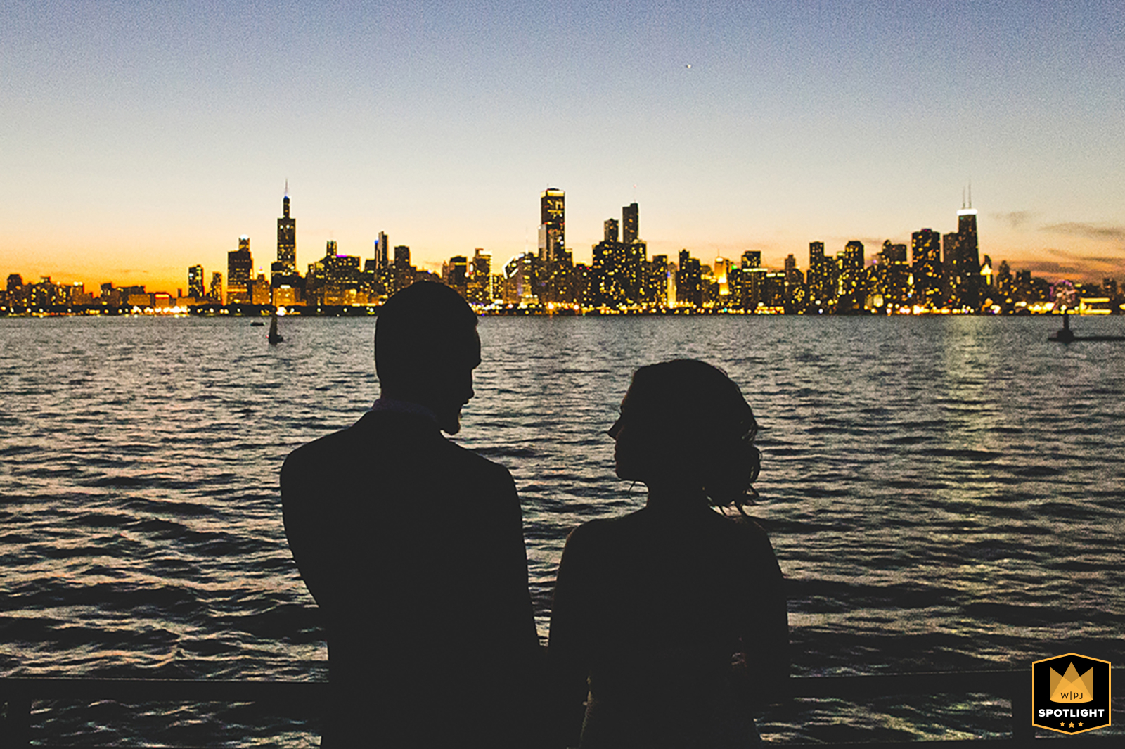 On the shores of Lake Michigan, IL, the bride and groom pose at night with the stunning Chicago skyline illuminated in the background, highlighting a memorable urban romance.