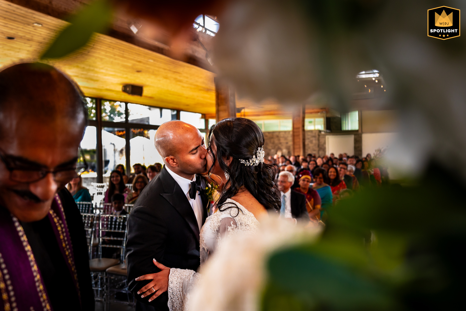 A wedding photograph shows a bride kissing the groom. The couple is at the altar at The Guild Inn. 