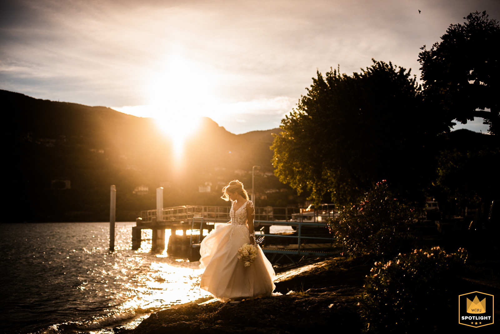 Sunset Serenity: Bride Strolls Beach During Romantic Isola Pescatori Wedding at Lake Maggiore A bride walks a beach at sunset on Isola Pescatori, Italy's Lake Maggiore. The photo captures a romantic moment during a wedding celebration.