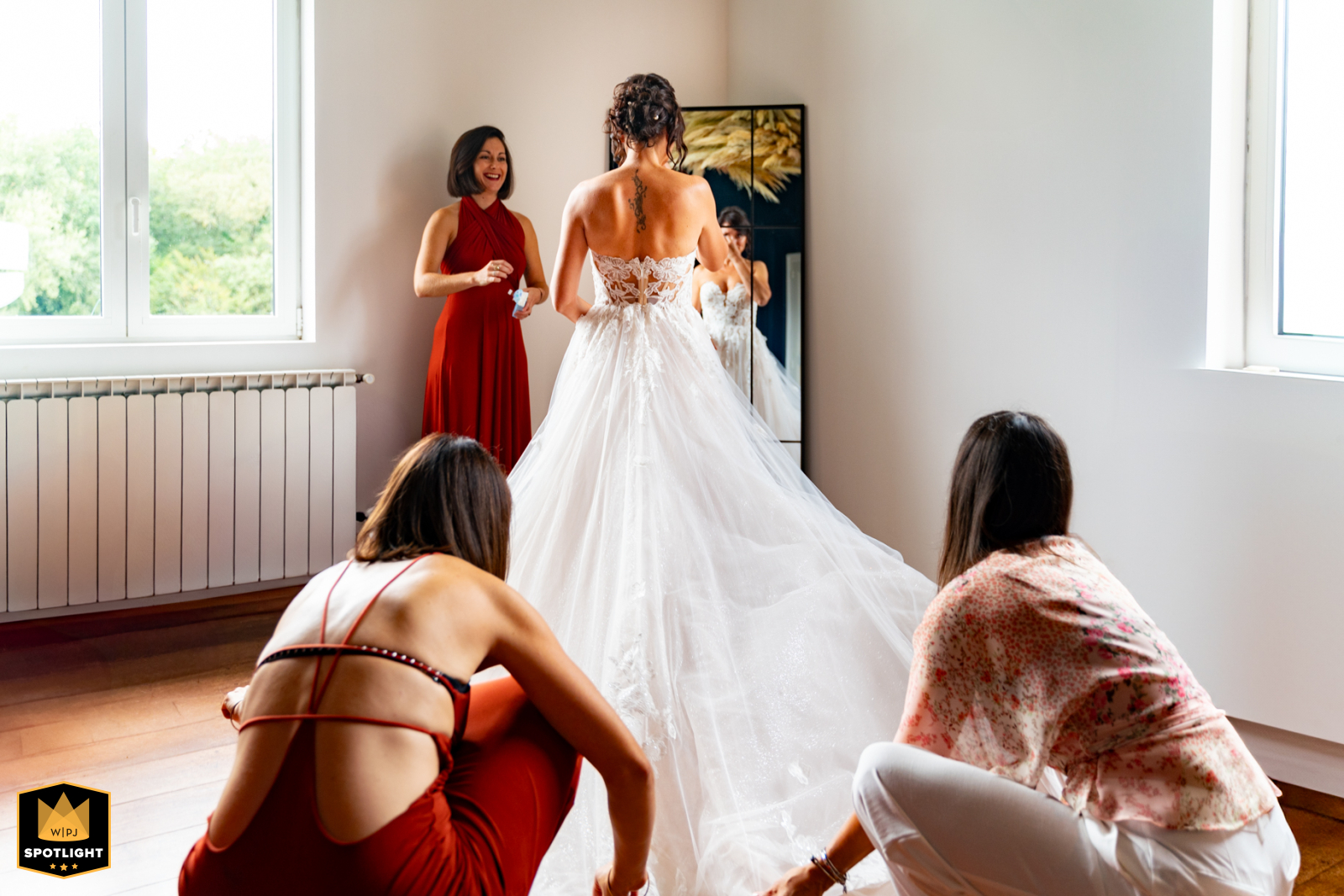 Nouvelle-Aquitaine: Bridesmaids Dress Bride by Mirror A WPJA wedding photo: Bridesmaids dress the bride in Nouvelle-Aquitaine, her gown fanned out, as she gazes into a full-length mirror.