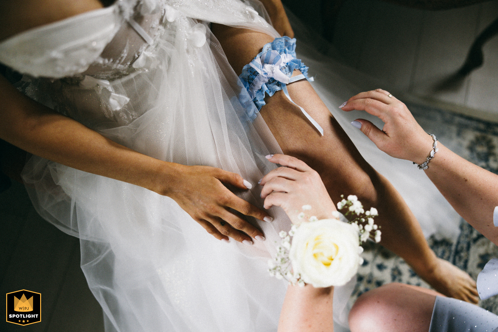 Bridesmaid and Garter in West Pomeranian A WPJA wedding photo: In West Pomeranian, Poland, a bridesmaid puts the garter on the bride, focusing on hands, arms, and one leg.