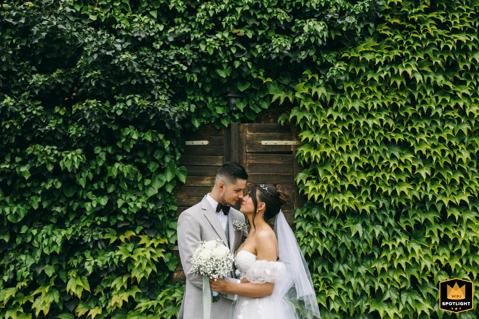 West Pomeranian: Couple Framed by Ivy Wall Next to the hotel in West Pomeranian, Poland, the bride and groom stand face-to-face during their reception session, framed by an ivy wall of green foliage.