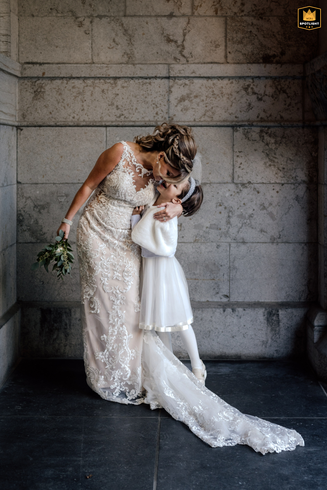 Downtown Montreal Portrait: Bride and Daughter Embrace In Downtown Montreal, QC, Canada, a bride and her daughter embrace indoors against a stone wall during portraits.