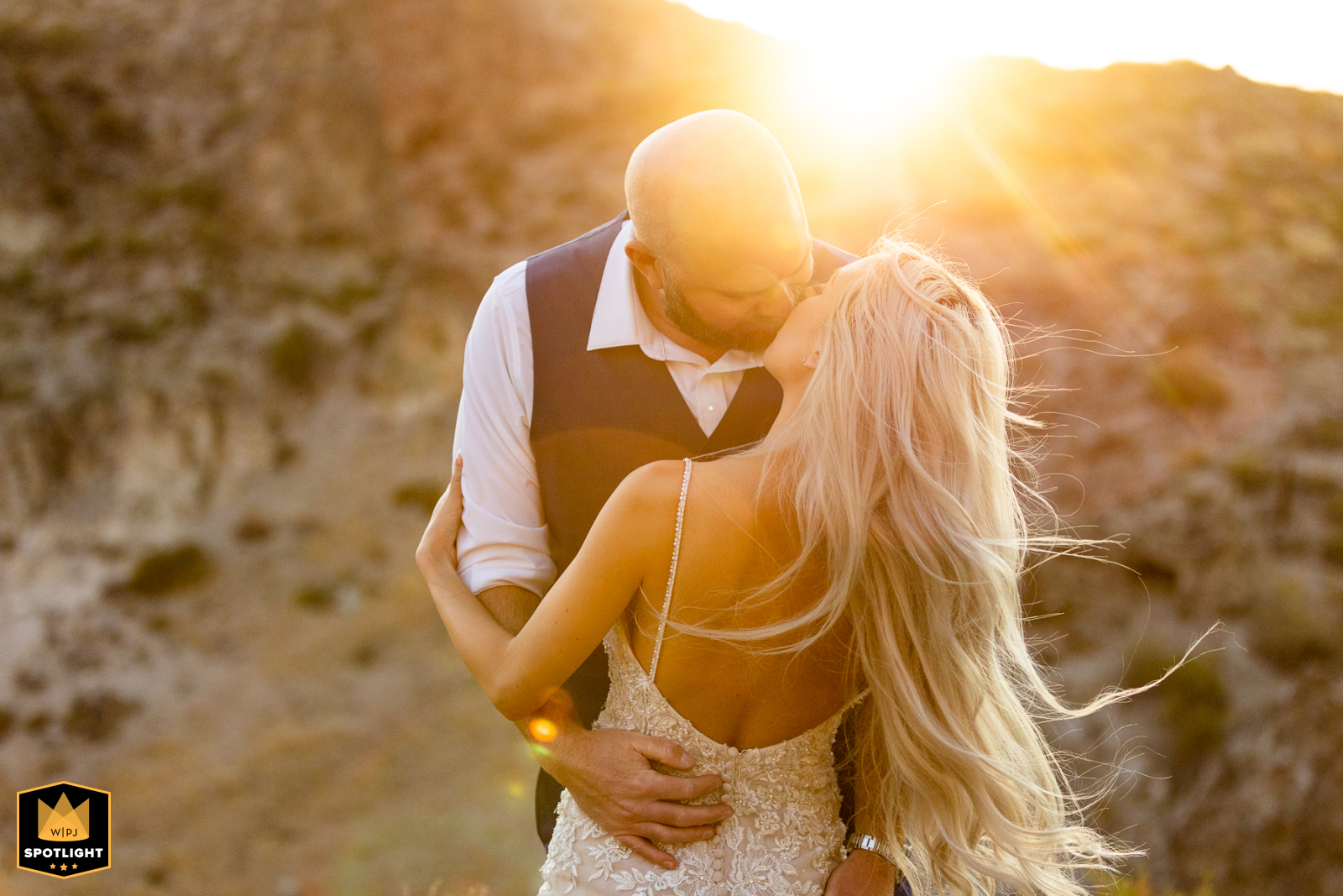 In Hot Springs, Mammoth Lakes California, the groom gives his bride a romantic kiss, her hair blowing in the warm, glowing sunset breeze.