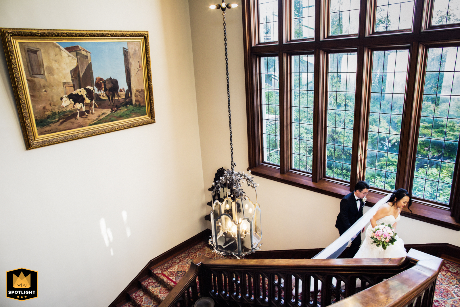 At Kohl Mansion in Burlingame, CA, the bride and groom ascend grand stairs below tall, elegant windows during their reception.
