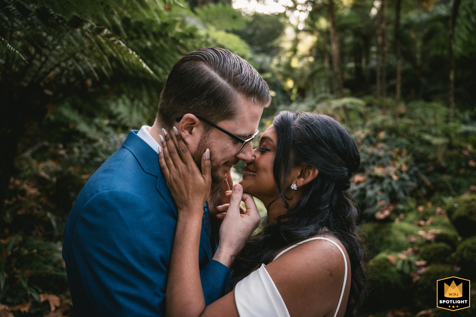 In Sintra, Portugal, a couple shares a kiss in a green, mossy forest. They pose face to face, captured in a romantic and enchanting natural setting.