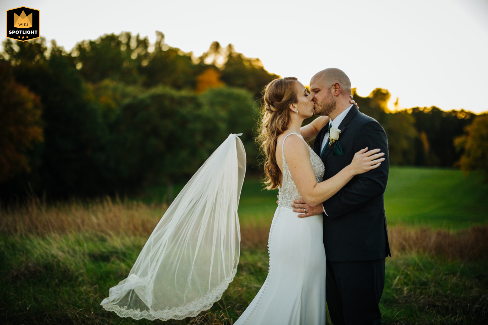 In Rockland County, New York, a couple shares a tender kiss during golden hour. As the sun glows softly, the bride’s veil slips free, creating a candid, joyful image that captures the spontaneity and romance of their day.