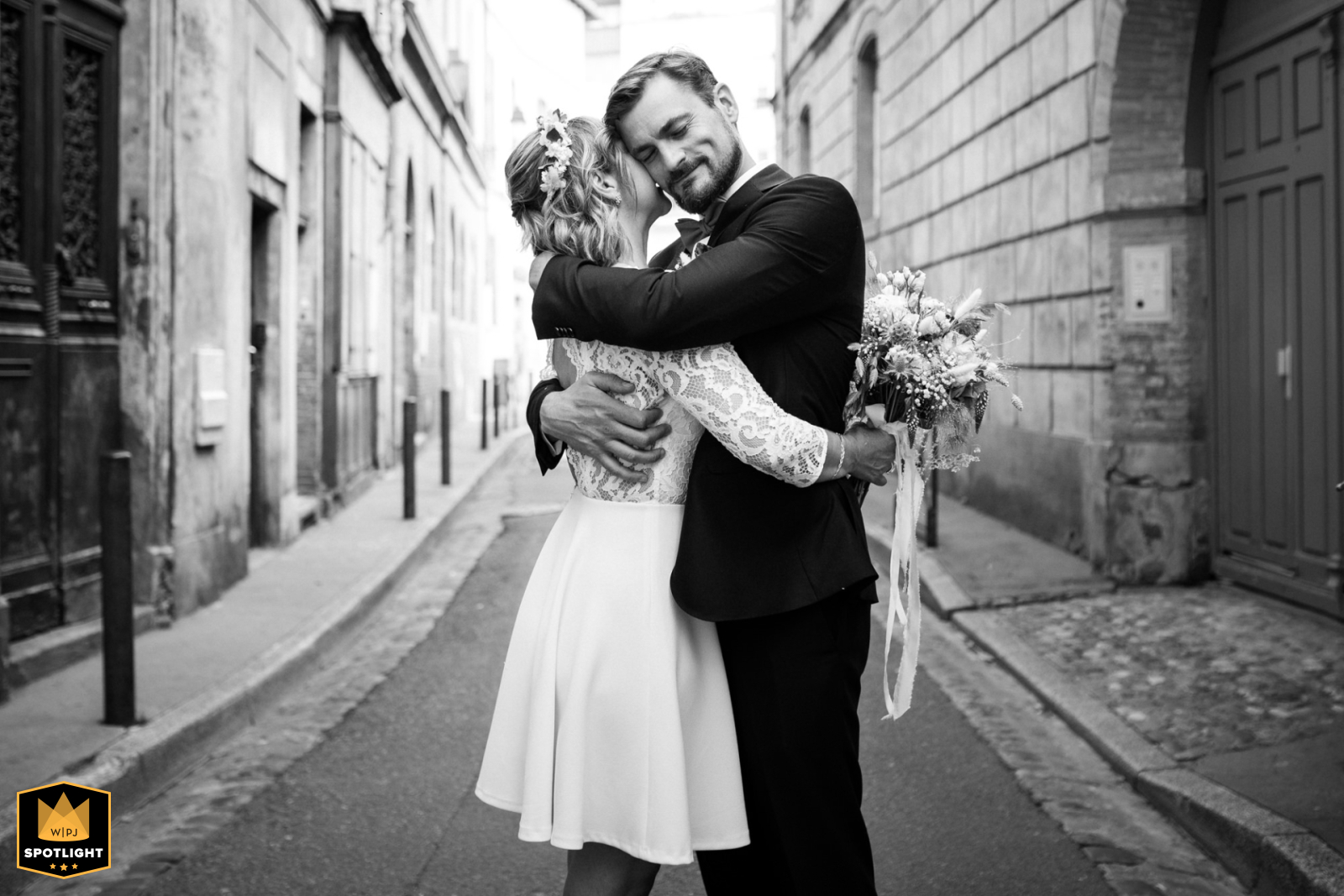 In a quiet urban alley in Toulouse, Haute-Garonne, a couple shares a loving embrace, captured in black and white. Their hug radiates tenderness and intimacy, creating a timeless portrait of love amid city surroundings.