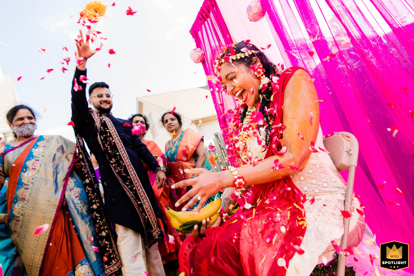 In Schaumburg, IL, the bride sits radiant during her haldi ceremony, a cherished Indian wedding tradition. Loved ones shower her with flower petals, filling the air with color and joy, celebrating love, blessings, and new beginnings.