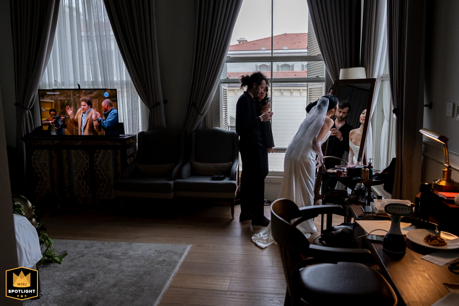 Unveiling Beauty, A Bride's Stillness, Pistol-Poised Freeze Frame in View At Six Senses Kocataş Mansions, İstanbul, a WPJA photographer captures a unique preparation moment. The bride checks her makeup as a television in the background shows a pistol and freeze frames.