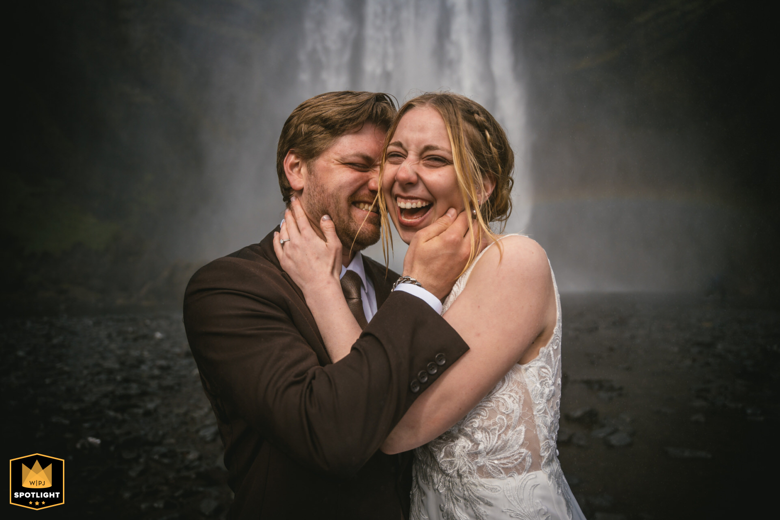 Skogafoss, Iceland: A joyful portrait of a bride and groom laughing heartily with the magnificent waterfall as their backdrop.