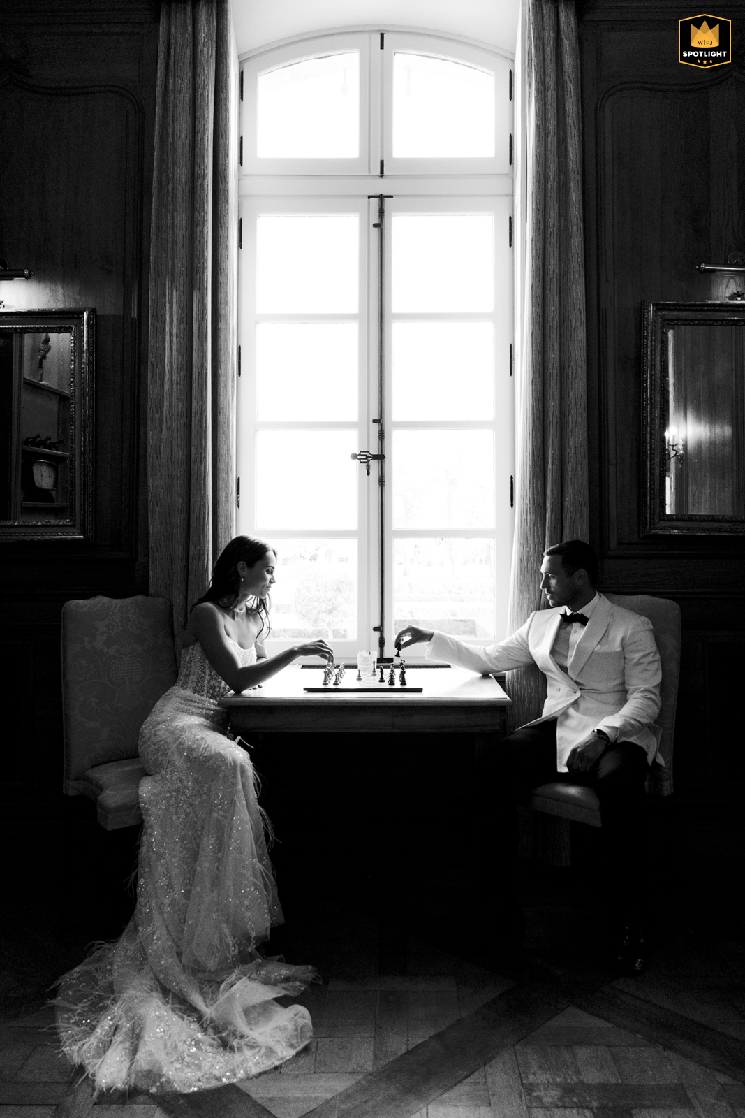 Bride And Groom Play Joyful Game By Window At Château De Tourreau The bride and groom play a game at a table by a window in Château de Tourreau.