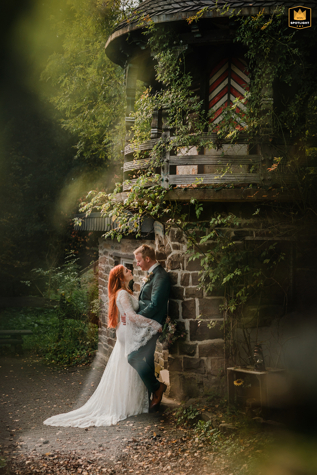 In Germany's Märchenwald Altenberg in Odenthal, the wedding couple poses for a dreamy, filter-enhanced portrait beside a stone tower within the atmospheric fairy-tale forest.