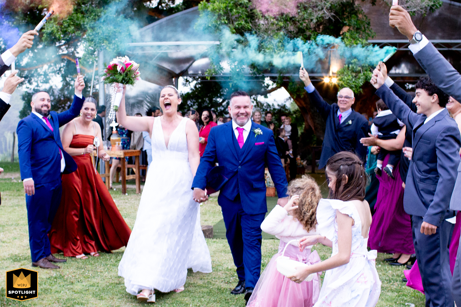 At FF - Espaço de Eventos, guests line the outdoor ceremony path holding vibrant smoke grenades, creating a festive cloud of color as the newlyweds exit, celebrating with infectious joy and excitement.