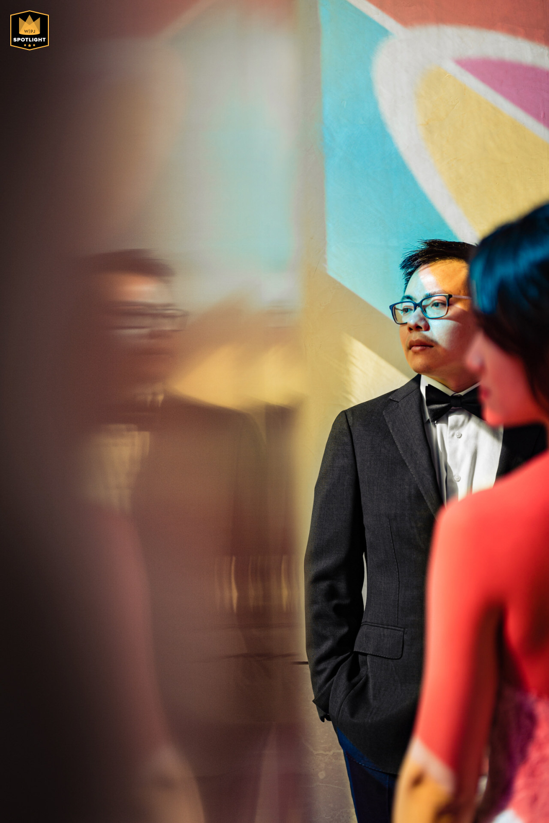 At Top of the Rock in New York City, the groom stands with bride patiently in front of a vibrant, colorful wall painting, bathed in bold hues, bringing an artful and stylish energy to this contemporary, urban wedding portrait.