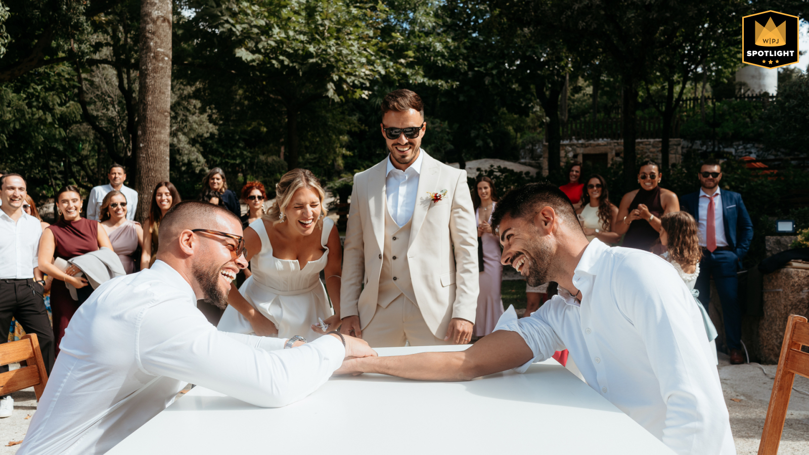 Two Men Arm Wrestling Over Whiskey Bottle Surrounded By Laughing Guests In Esposende, Portugal, two men smile and compete in a lively arm wrestling match over a bottle of whiskey, surrounded by laughter and cheers, highlighting the playful spirit and camaraderie of the wedding celebration.