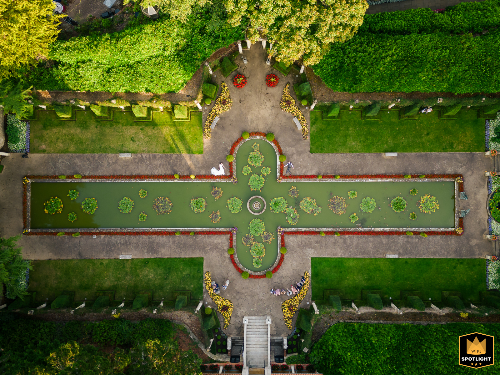 At The Italian Villa in Dorset, UK, the bride and groom pose playfully near the pond for a drone portrait, amid the elegant landscape captured from above, showcasing their lighthearted spirit amid the villa’s picturesque grounds.