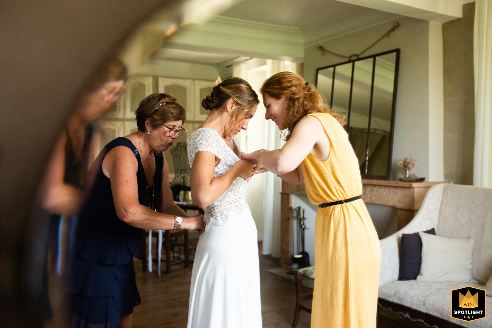 At Château de Launac in Haute-Garonne, the bride is captured during her preparations, her reflection beautifully framed in a beveled-edge mirror that artfully echoes its shape, highlighting her focused expression in the elegant setting.