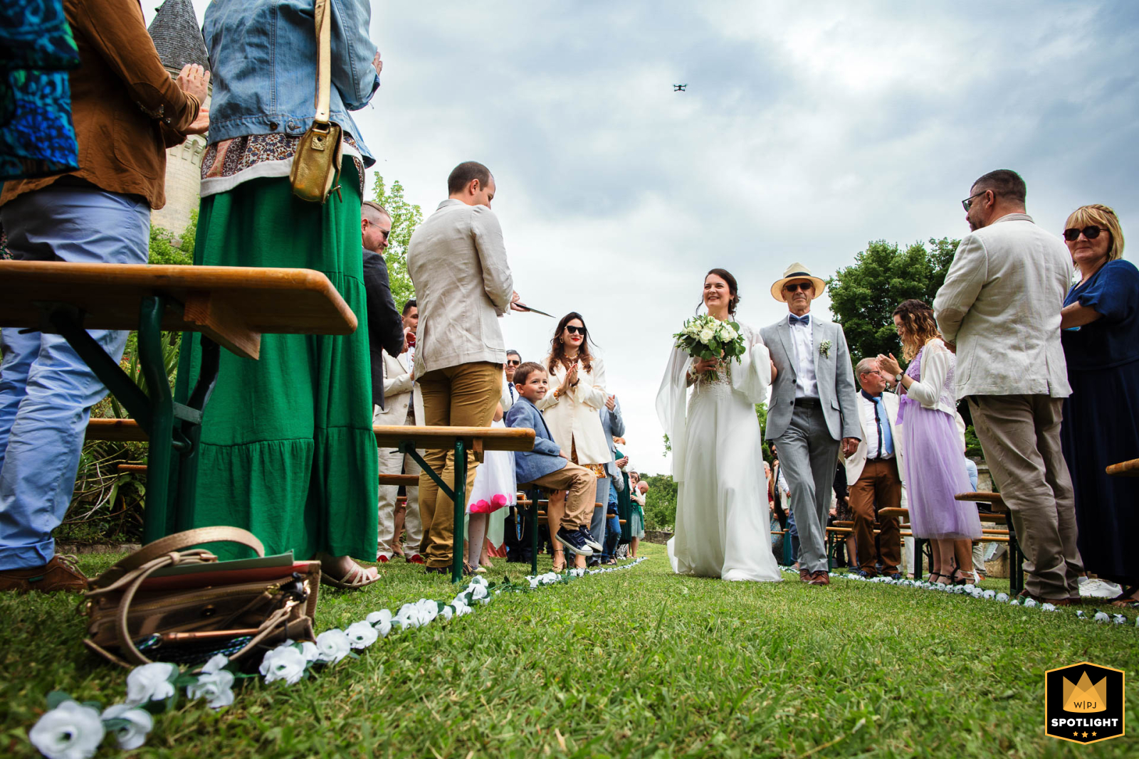   The bride walks alongside her father at Château de Fléac, with guests turning to watch as she makes her way forward during the ceremony.
