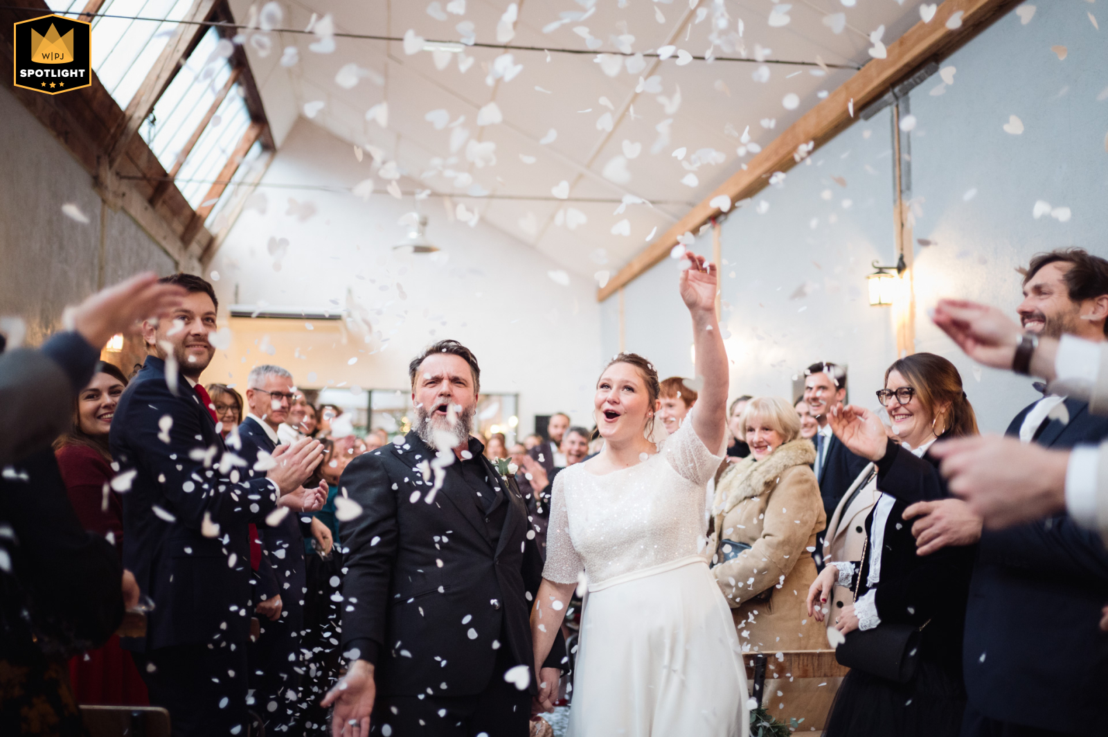  At La Factory in Thizy-les-Bourgs, Rhône, France, the couple celebrates their wedding exit beneath a cascade of confetti and joyful cheers from friends and family.
