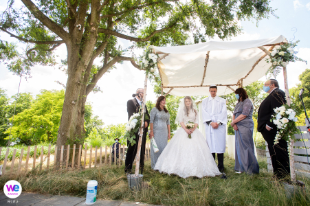 A small elopement ceremony was held outdoors on private property, with a chuppah embraced by a tree, captured in a wide angle shot