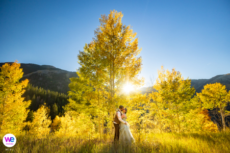 Couple shares first kiss as newlyweds, surrounded by golden fall hues on a mountain.