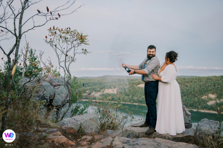 As the sun sets over Cleopatra's Needle in Baraboo, Wisconsin, Kayla and Landen celebrate their elopement by joyfully popping a bottle of champagne, capturing a perfect moment of love and celebration.