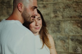In front of an old stone wall, a couple poses during their engagement session in Tuscany, capturing the charm and beauty of the region's Old World architecture and history.