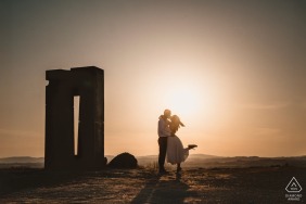 The couple stands in Crete Senesi, Tuscany, embracing each other in a romantic pose. As the sun sets behind them, the woman gracefully lifts her leg, captured by the wedding photographer.