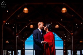 An artistic portrait captured by a skilled WPJA photographer, as the engaged couple stands in a serene Ontario Trail Hub, bathed in natural light and a hint of added flash. They embrace lovingly, framed against a dark background.