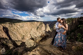 At Black Canyon of the Gunnison National Park, CO, a couple poses on the canyon's edge. The dramatic clouds accentuate the breathtaking vista from their perch.
