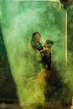 In Pavagadh, Gujarat, India, a couple poses for a vibrant pre-wedding engagement portrait amidst the dramatic effect of a colorful green smoke grenade, adding an enchanting and lively atmosphere.