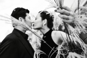 This photo captures an engaged couple at the Bund in Shanghai, China. The bride-to-be is holding a cluster of reeds while both she and her partner are dressed in all black, creating a romantic and timeless black and white shot.