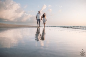 Couple walking on a water mirror at the beach during sunrise in Maceió, Brazil, captured by a wedding photographer.