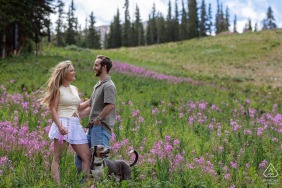 An engaged couple is nestled among colorful summer flowers on a scenic ski run at Arapahoe Basin Ski Area, Colorado, enjoying the vibrant high-altitude beauty of the mountains.