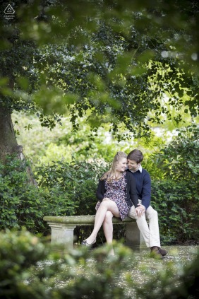 This engagement portrait features a couple sitting together in London, UK, showcasing their deep bond amidst trees in a park setting.