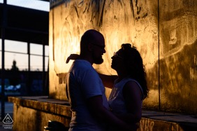 This couple shares a warm embrace against a sunlit concrete wall in Eindhoven Strijp-S, Netherlands, as soft light reflects off the surface to create a beautiful engagement portrait.