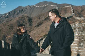 The couple stands together against the historic stone architecture of the Mutianyu Great Wall in Beijing, China, representing an enduring love that spans through time at this iconic landmark.