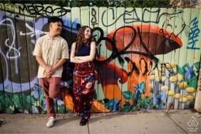 This fun engagement portrait features a couple posing with vibrant street art in the Logan Square neighborhood of Chicago, Illinois, showcasing their personality against a colorful urban backdrop.