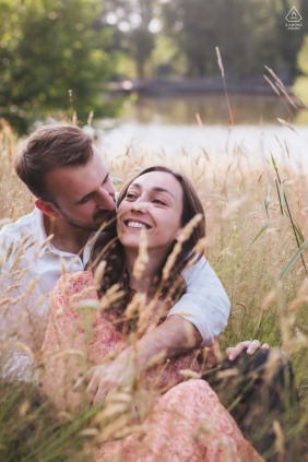 The fiancé tenderly kisses his partner's neck as they lie closely together in a scenic field at Lacs d'Halco in Landes, France, during a peaceful and intimate engagement session.