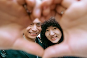This joyful couple shares a cheerful interaction in Kaifeng, Henan, smiling brightly while using their hands to form a heart shape during their lighthearted and romantic engagement session in China.