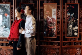 A young man and woman stand together in Kaifeng, Henan, gazing forward in front of a traditional Chinese screen during their elegant and culturally inspired engagement portrait session in China.