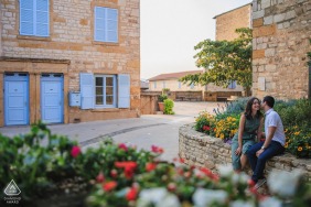 The couple shares a quiet kiss in a charming village in Beaujolais, Rhône, France, surrounded by rustic stone textures and blooming colors during their picturesque and traditional engagement portrait.