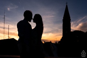 A striking silhouette of the couple is captured alongside a historic bell tower in Caorle, Venice, Italy, highlighting their connection against the scenic coastal skyline of this beautiful region.