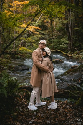 In Aomori, Japan, the couple poses in the forest during the vibrant fall season, colorful leaves carpeting the ground and overhead branches, their connection highlighted by the beauty of nature’s changing colors.